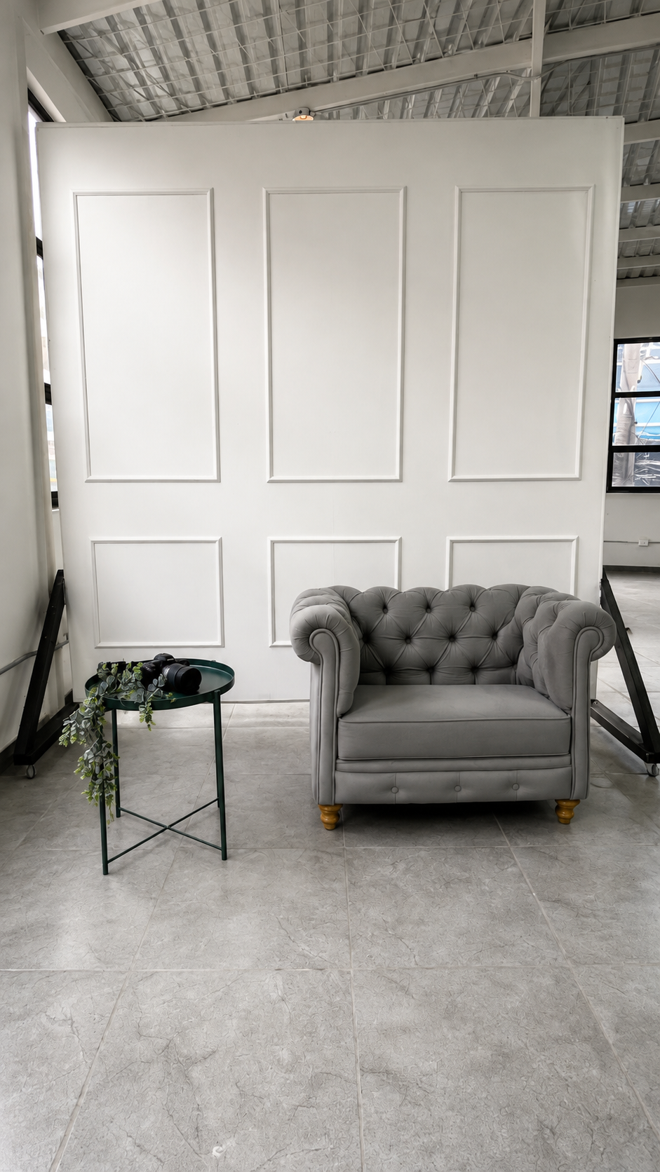 Set con poltrona gris capitonée y mesa auxiliar sobre fondo blanco panelado — L'ATELIER 64